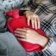 Person holding a hot water bottle over their abdomen while lying down