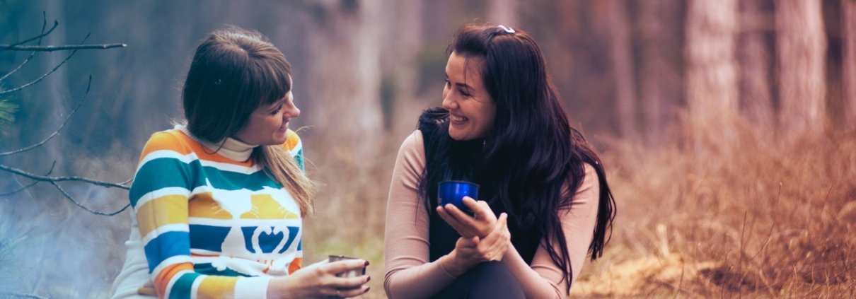 Two women sitting in front of a campfire and talking with each other