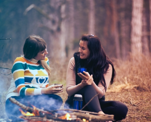 Two women sitting in front of a campfire and talking with each other