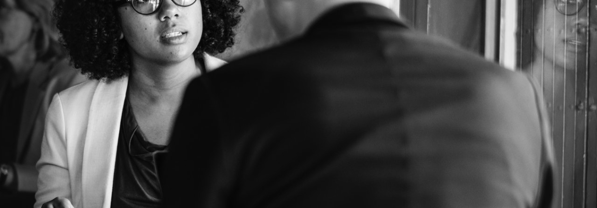 Woman sitting in a cafe facing a man with angry look whose back is to camera.