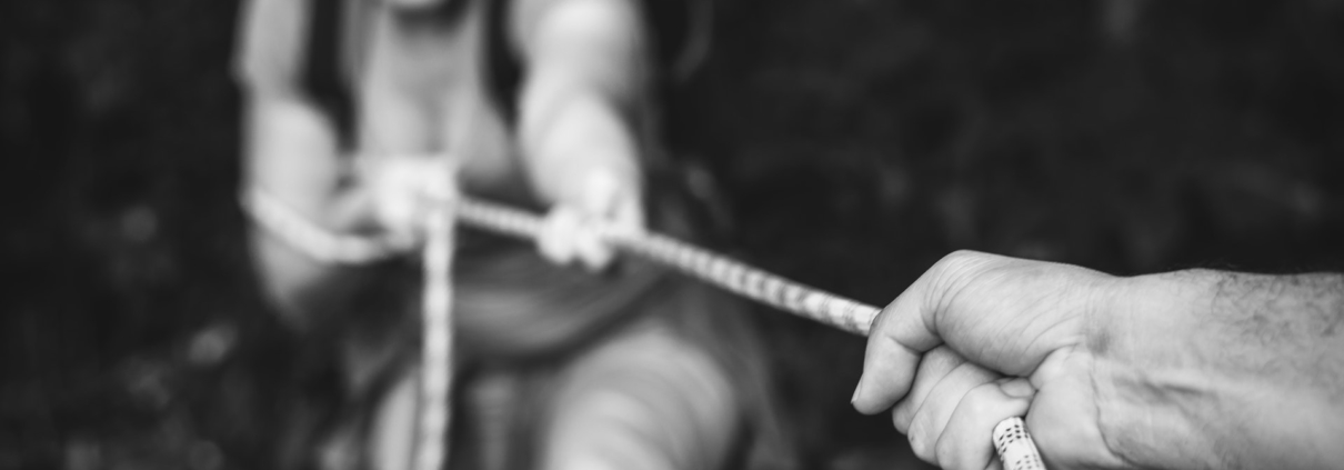 Blurred image of a hand holding a rope to support a woman climbing up