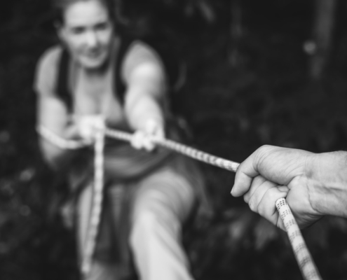 Blurred image of a hand holding a rope to support a woman climbing up