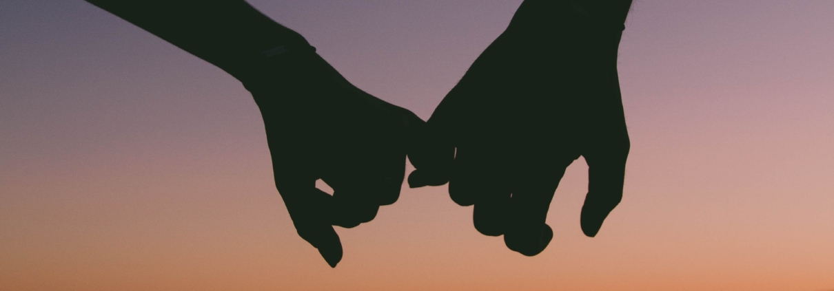 Silhouette of two hands with little fingers linked in front of an ocean sunset