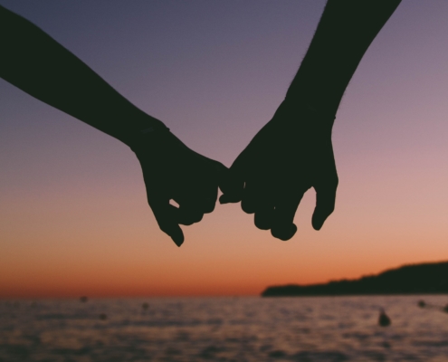 Silhouette of two hands with little fingers linked in front of an ocean sunset