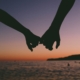 Silhouette of two hands with little fingers linked in front of an ocean sunset