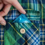 Hand putting a condom in the pocket of a blue and green checked shirt