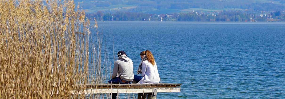 Man and woman sitting on a jetty over a lake and talking