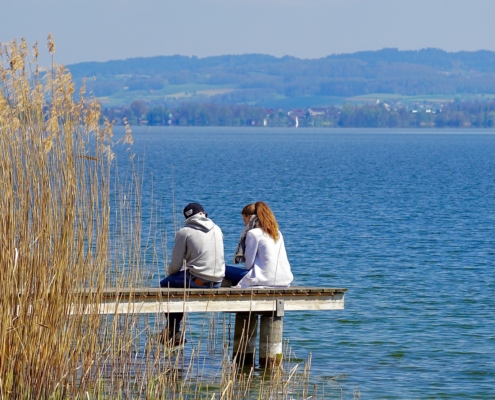 Man and woman sitting on a jetty over a lake and talking
